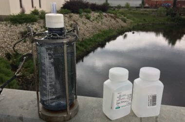 Bottles for water testing sit on the ledge by a small body of water