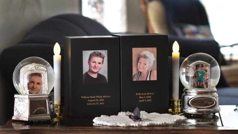 An end-table memorial for William McIver and Kelly McIver featuring a candle for each and photos of each.