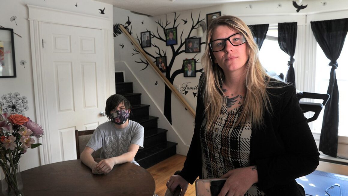 Courtney Allen poses for a photo while standing next to the dining table that her son is sitting at.