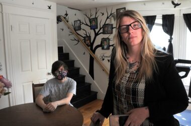 Courtney Allen poses for a photo while standing next to the dining table that her son is sitting at.