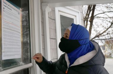 Hibo Omer reads a notice of environmental lead hazards sign that is affixed to the glass of a home in Lewiston