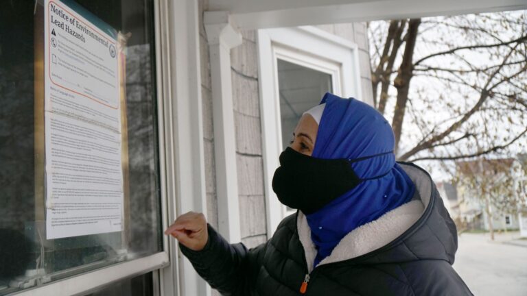 Hibo Omer reads a notice of environmental lead hazards sign that is affixed to the glass of a home in Lewiston