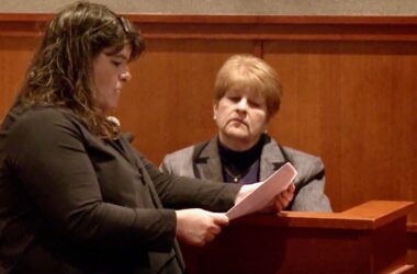 Amy Fairfield reads a paper while standing in front of the witness stand within a courtroom