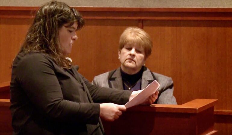 Amy Fairfield reads a paper while standing in front of the witness stand within a courtroom