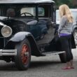 A blonde woman admiring a black antique car