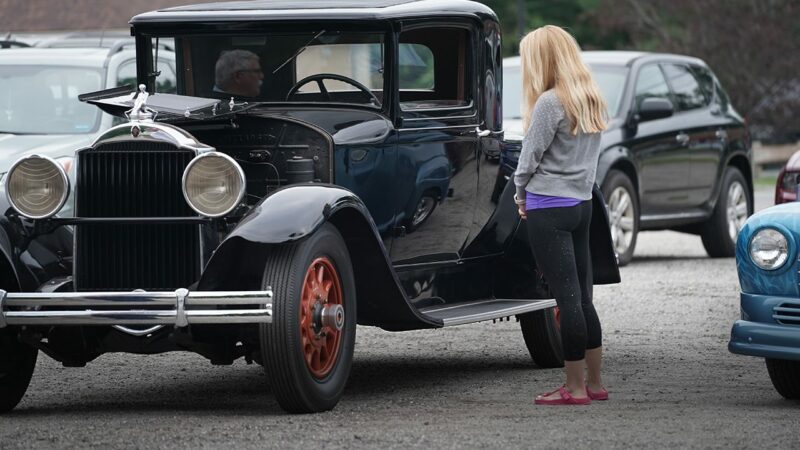 A blonde woman admiring a black antique car