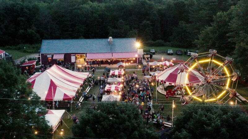An aerial view of the Casco Days fair, with tents, a merry-go-round and a ferris wheel.