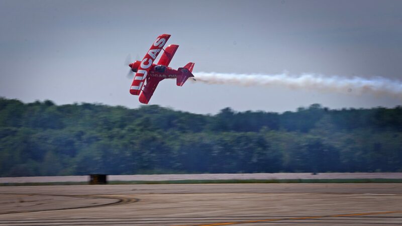 A red plane flies through the air during an air show.