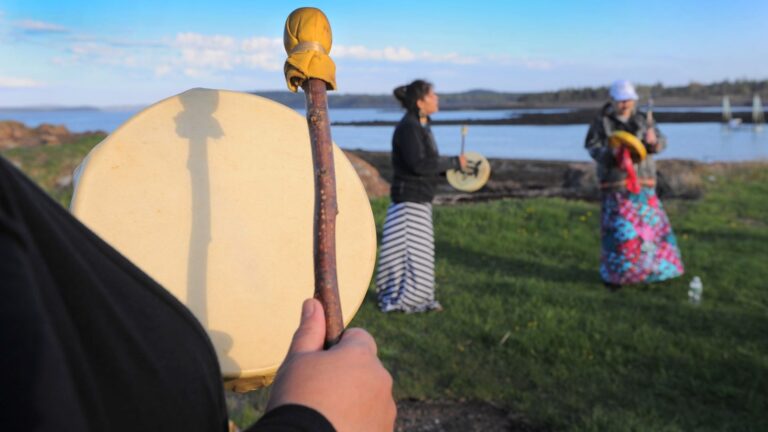 A group of three women beat hand-held drums as part of a Passamaquoddy cultural event