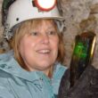 Mary Freeman, wearing a head lamp, smiles while looking at a piece of tourmaline