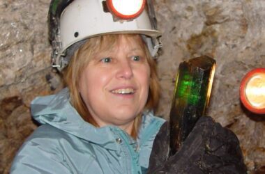 Mary Freeman, wearing a head lamp, smiles while looking at a piece of tourmaline