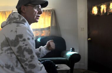 Steven Clarke sits in a motel room while he speaks with an individual not shown in the photo.