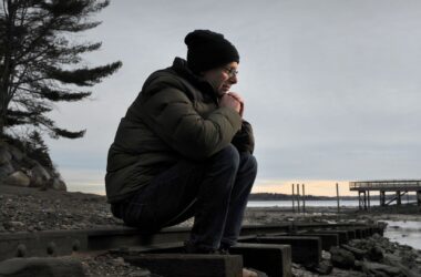 Steven Clarke sits on railroad tracks with his chin resting on his closed hands as he rests his arms against his knees.