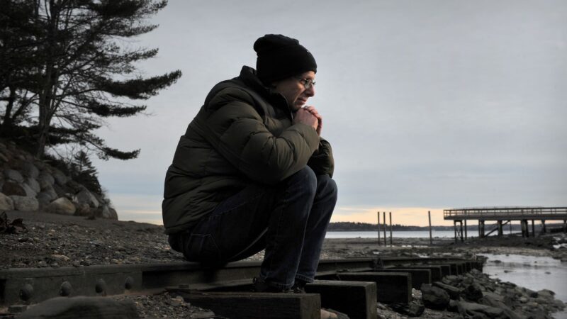 Steven Clarke sits on railroad tracks with his chin resting on his closed hands as he rests his arms against his knees.