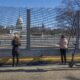 A group of four individuals looks at the U.S. Capitol, which is now protected by fence barriers.