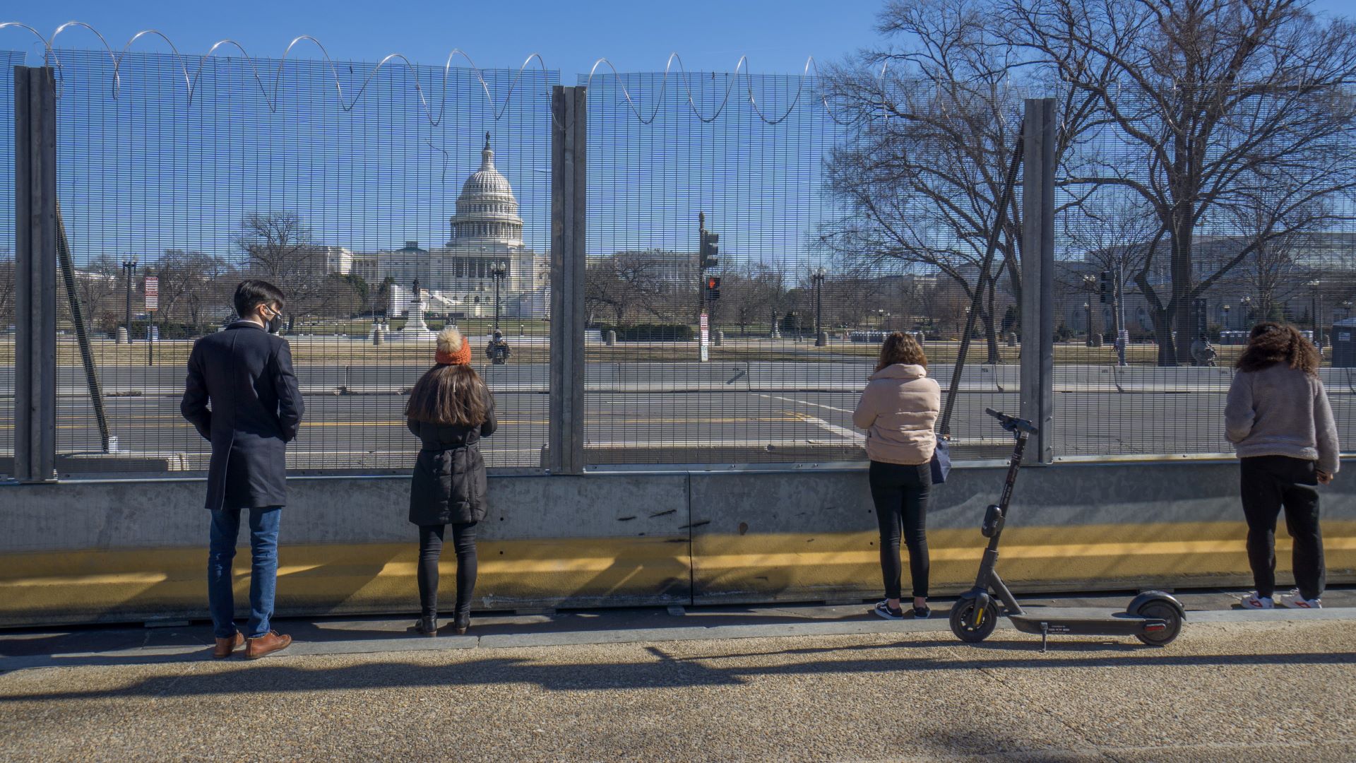 A group of four individuals looks at the U.S. Capitol, which is now protected by fence barriers.