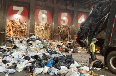 A garbage truck prepares to dump bags of trash in a warehouse