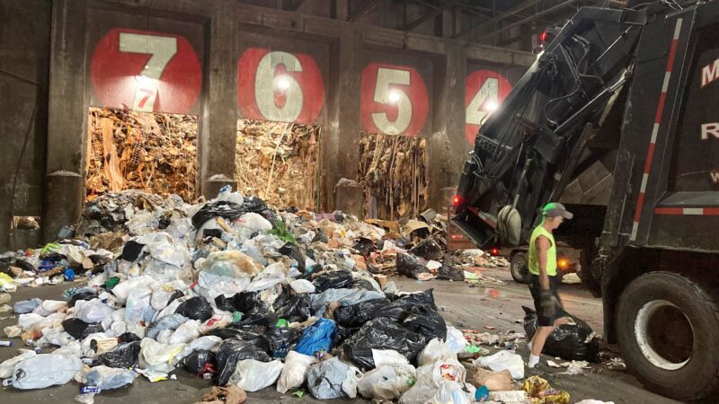 A garbage truck prepares to dump bags of trash in a warehouse