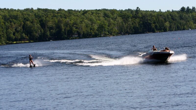 An individual rides on water skis while being pulled by a speed boat