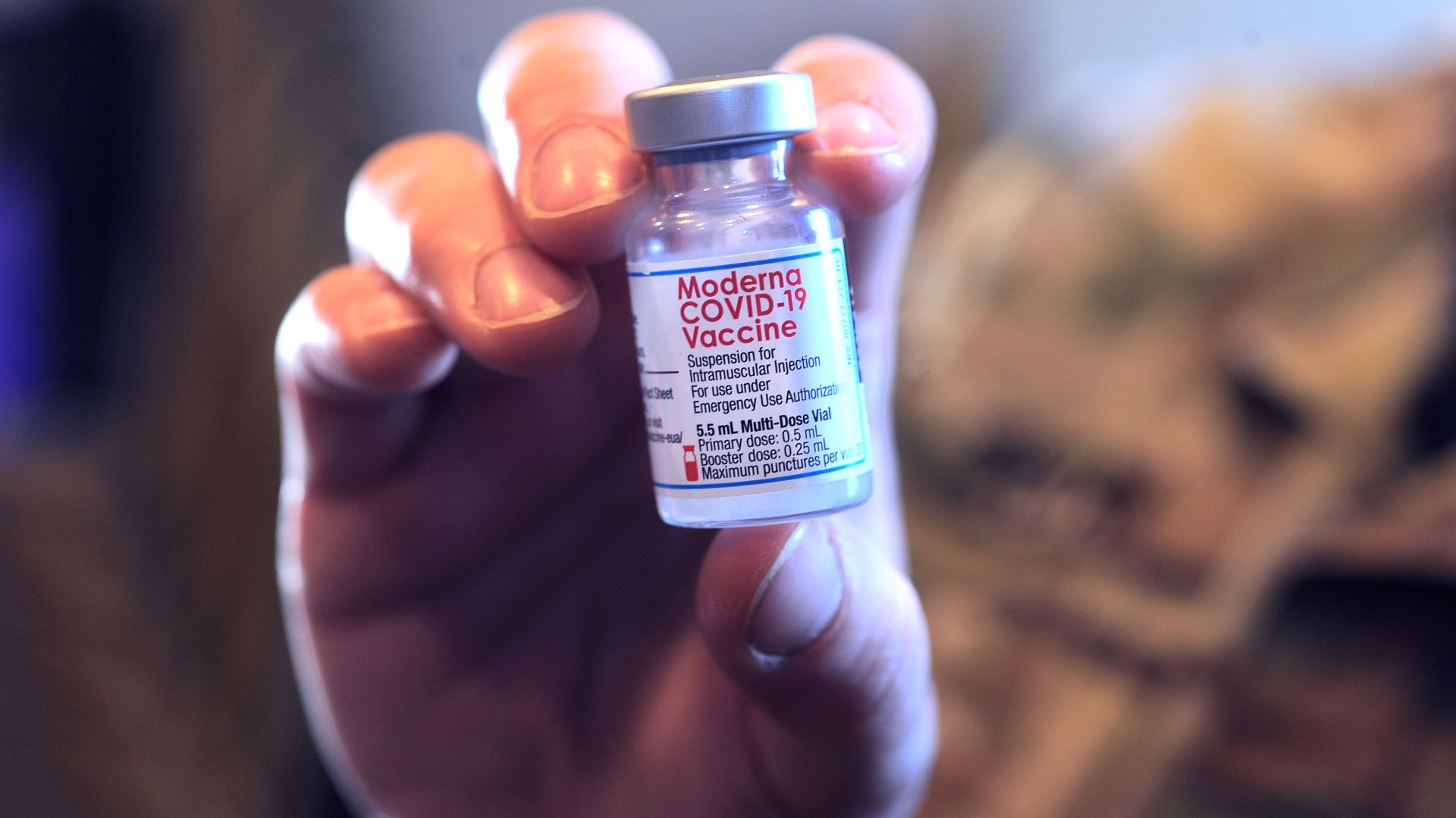 A hand holds up a small vial of a COVID-19 vaccine