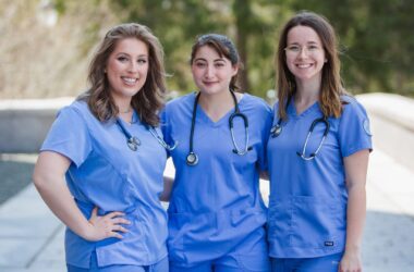 A group of three smiling women, each wearing nursing scrubs with a stethoscope around each of their necks