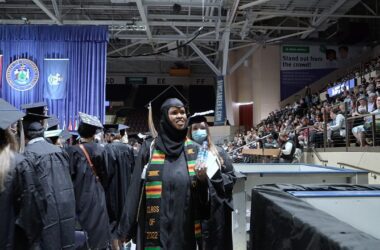 A university graduate wearing a cap and gown walks past other graduates during a graduation ceremony