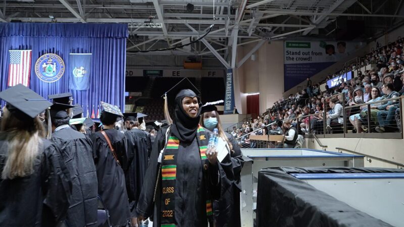 A university graduate wearing a cap and gown walks past other graduates during a graduation ceremony