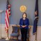 Maine Secretary of State Shenna Bellows stands between the U.S. Flag and State of Maine flag in her office.