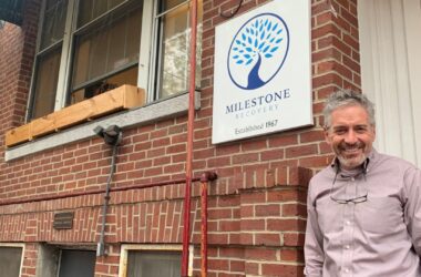 Tom Doherty, executive director of Milestone Recovery, smiles while standing underneath the organization's logo outside its offices