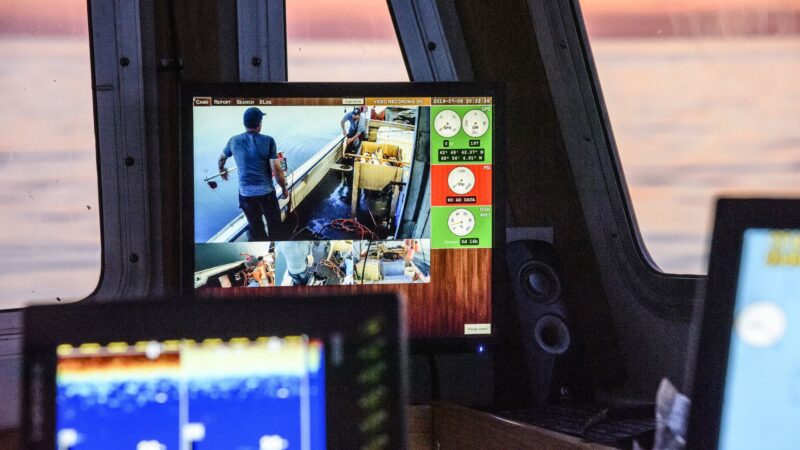 A screen displays a live feed of a camera that is monitoring fishermen aboard a boat