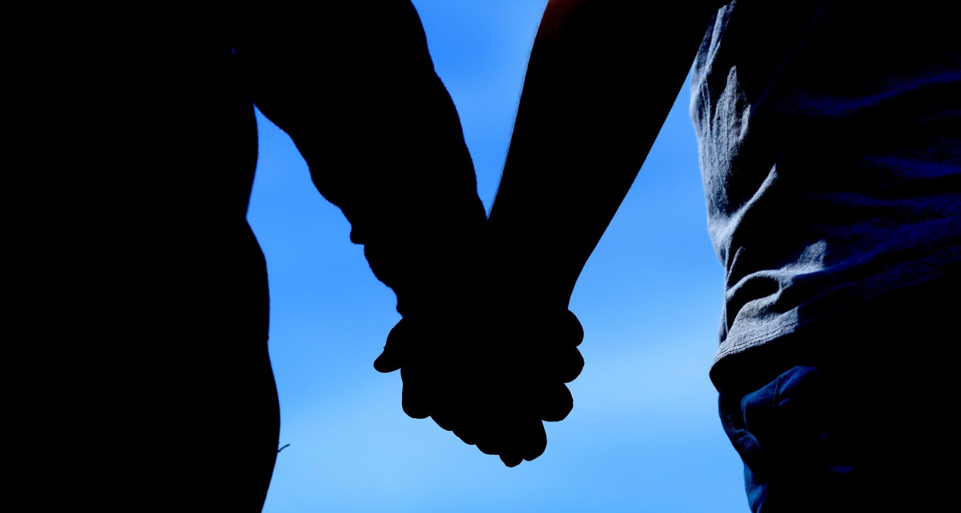 A silhouette image of two individuals holding hands