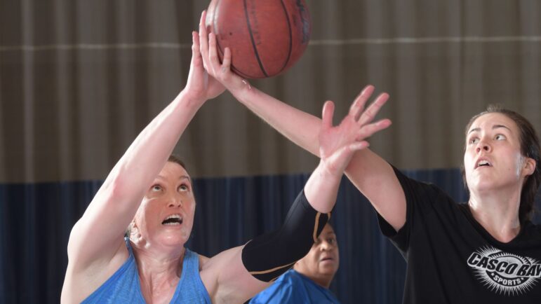 Two women each attempt to rebound a basketball