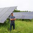 Seth Kroeck poses for a photo next to solar panels
