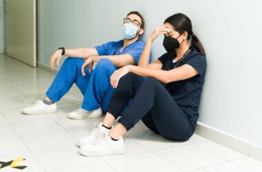 Two stressed out nurses, one a man and one a female, sit on the floor of a hospital