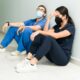 Two stressed out nurses, one a man and one a female, sit on the floor of a hospital