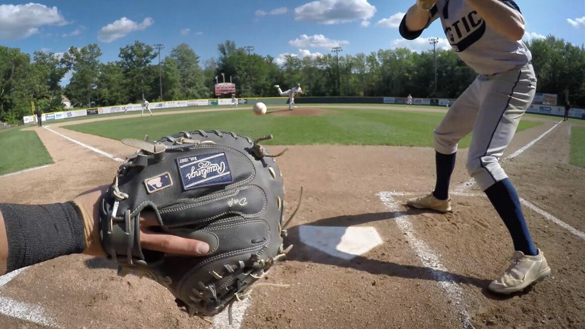 A baseball thrown by a pitcher prepares to land in the catcher's glove, sailing past the batter at right