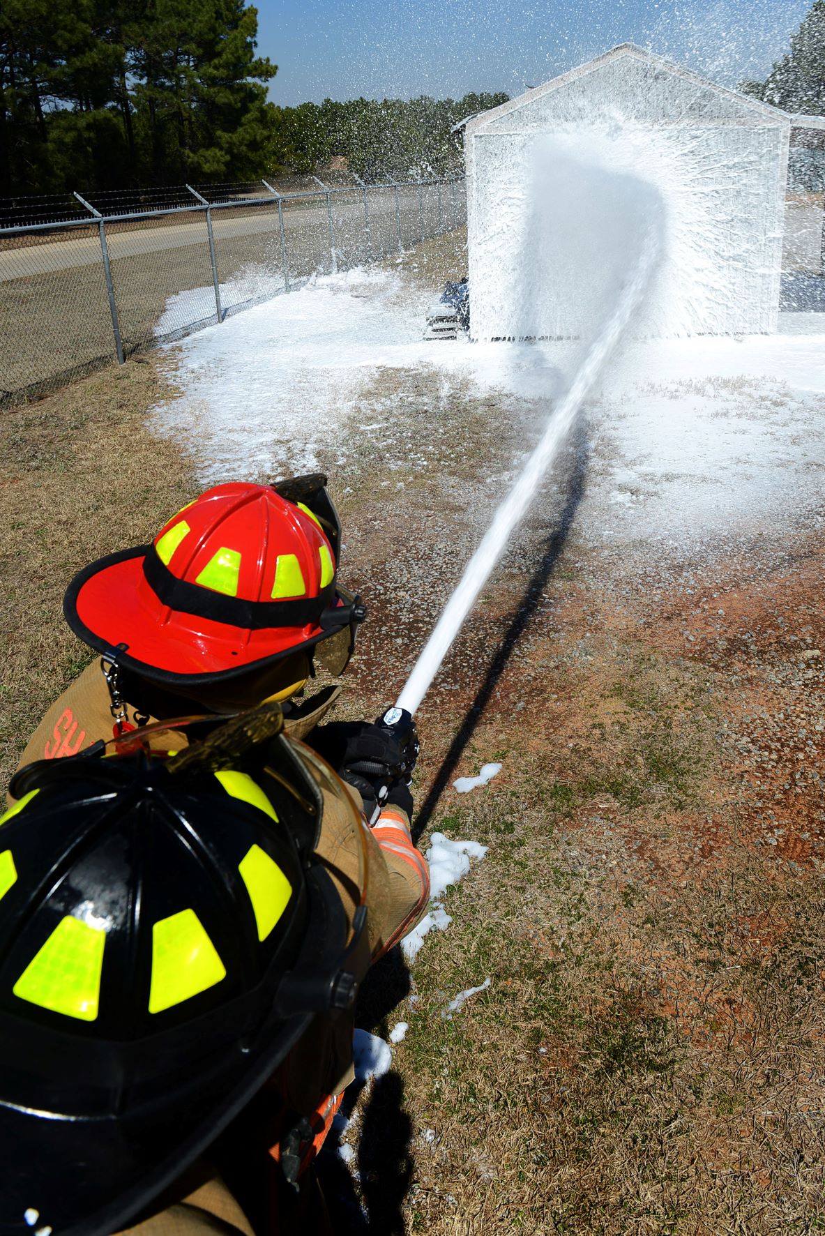 A pair of firefighters spray a shed with AAFF foam during a training excercise.