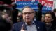 Paul LePage speaks during a campaign event with a crowd of people behind him, including some holding a red and blue sign that says LEPAGE GOVERNOR 2022