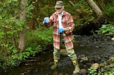 Martha Spiess stands in a brook to collect a water sample to assess PFAS contamination levels