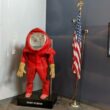 A red biohazard suit on display next to an American flag. The suit appears to be placed over a mannequin.