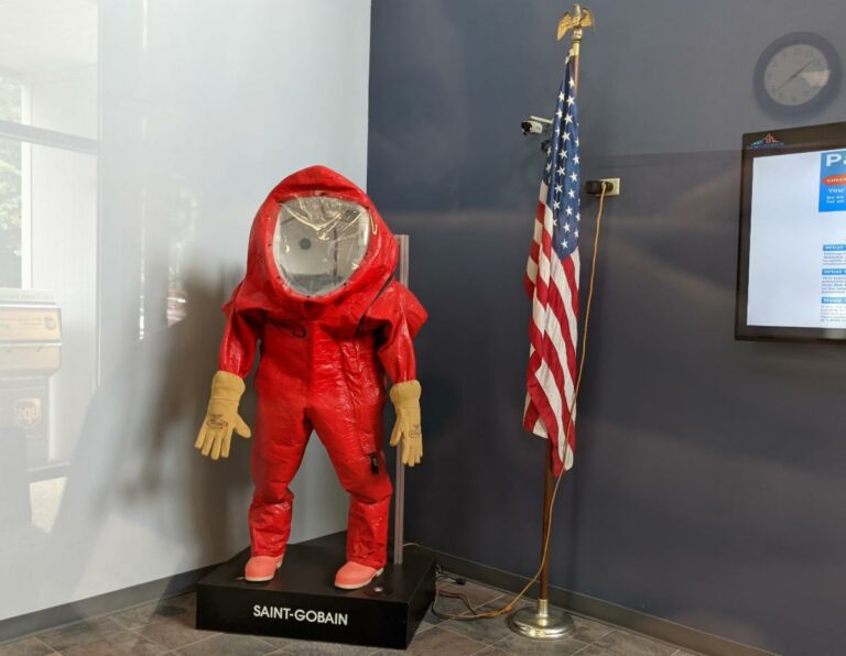 A red biohazard suit on display next to an American flag. The suit appears to be placed over a mannequin.