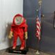 A red biohazard suit on display next to an American flag. The suit appears to be placed over a mannequin.