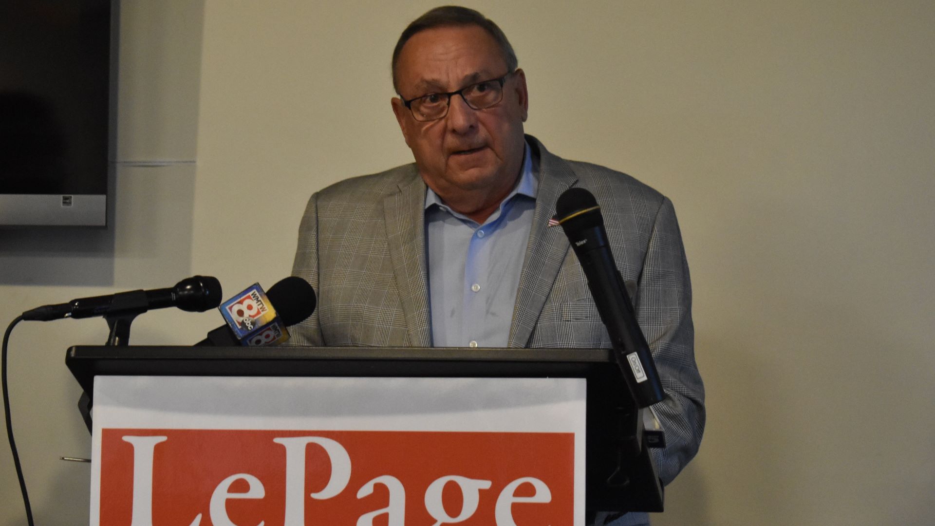 Former Maine Governor Paul LePage stands at a podium with microphones during a press conference.