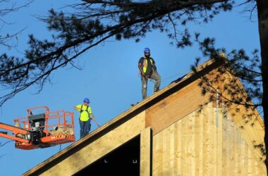 Two construction workers stand atop a roof made from timber