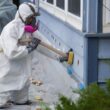 A man wearing a white protection suit injects insulation into the exterior wall of a home.