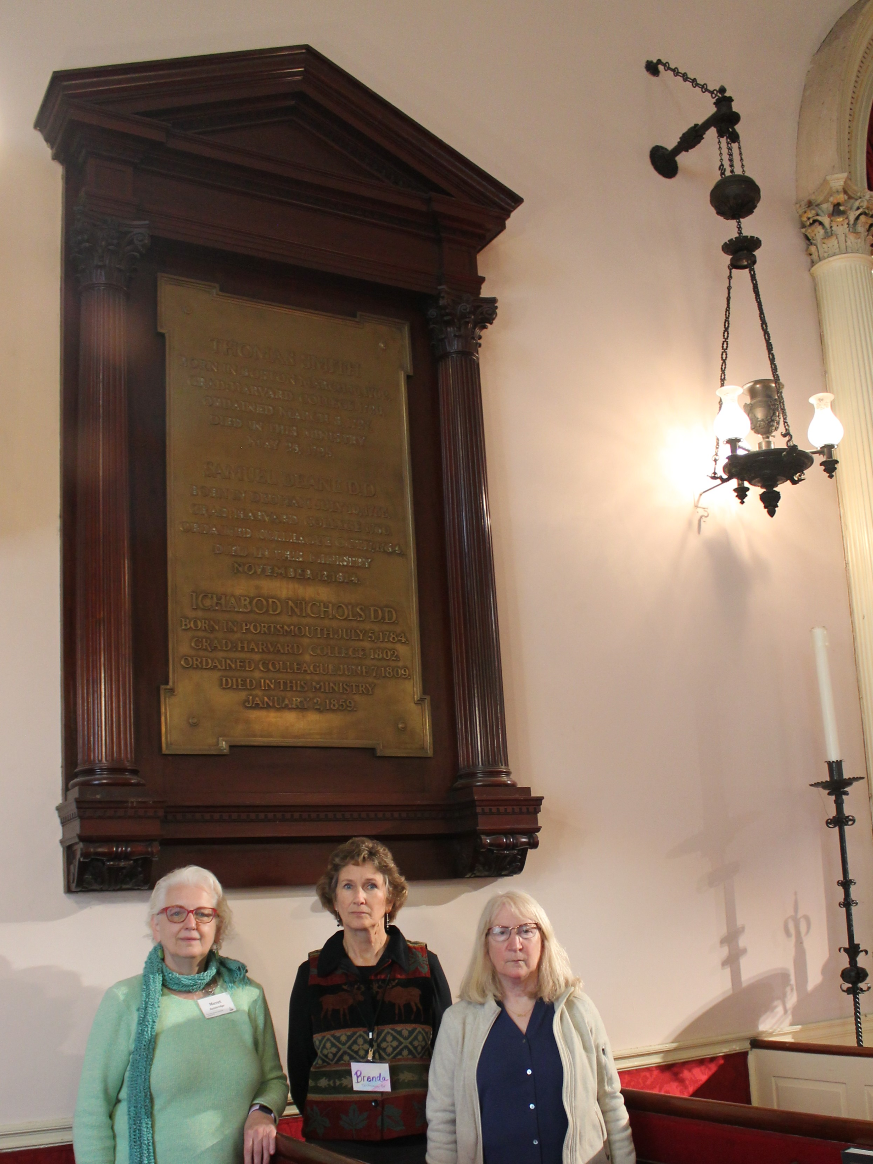 Three women stand in front of a large plaque.