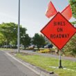 An orange transportation sign along the side of a road that reads "Bikes on Roadway"