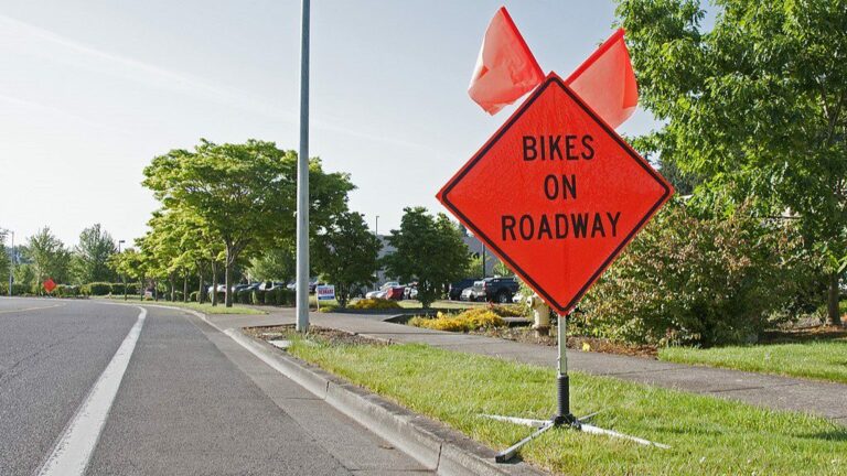 An orange transportation sign along the side of a road that reads "Bikes on Roadway"
