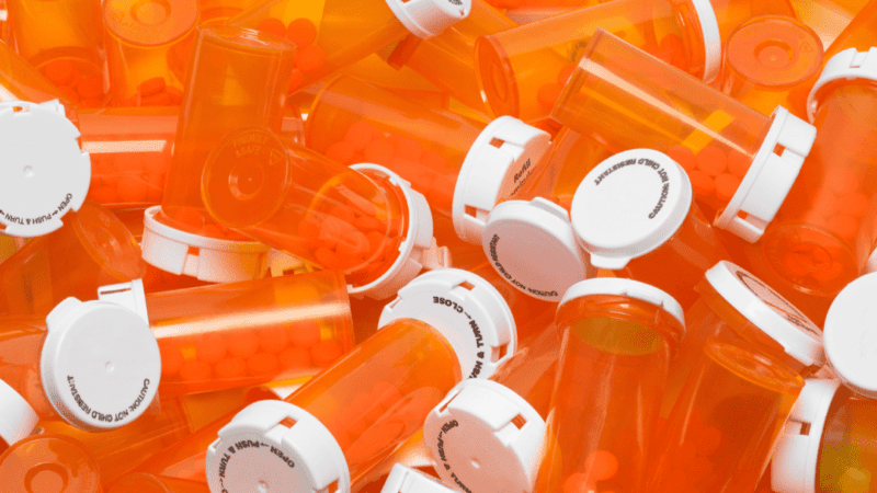 A pile of orange pill bottles with white caps and no labels