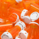 A pile of orange pill bottles with white caps and no labels